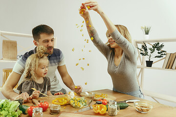 Image showing Cute little girl and her beautiful parents are cutting vegetables in kitchen at home