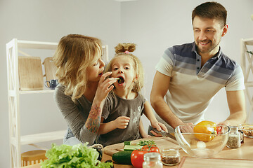 Image showing Cute little girl and her beautiful parents are cutting vegetables in kitchen at home