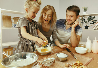 Image showing Cute little girl and her beautiful parents preparing the dough for the cake in kitchen at home