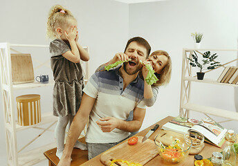 Image showing Cute little girl and her beautiful parents are cutting vegetables in kitchen at home