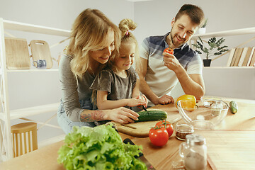 Image showing Cute little girl and her beautiful parents are cutting vegetables in kitchen at home