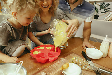 Image showing Cute little girl and her beautiful parents preparing the dough for the cake in kitchen at home