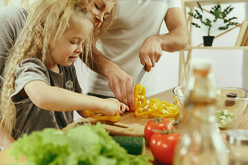 Image showing Cute little girl and her beautiful parents are cutting vegetables in kitchen at home