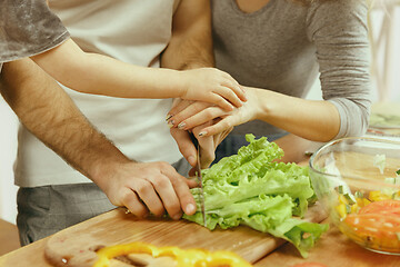 Image showing Cute little girl and her beautiful parents are cutting vegetables in kitchen at home