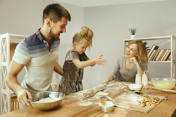 Image showing Cute little girl and her beautiful parents preparing the dough for the cake in kitchen at home