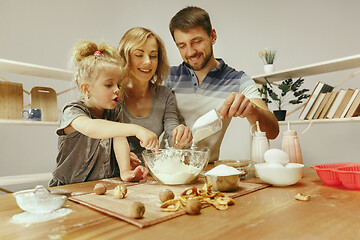 Image showing Cute little girl and her beautiful parents preparing the dough for the cake in kitchen at home