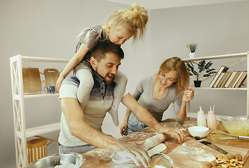 Image showing Cute little girl and her beautiful parents preparing the dough for the cake in kitchen at home