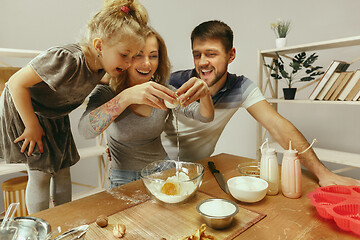 Image showing Cute little girl and her beautiful parents preparing the dough for the cake in kitchen at home