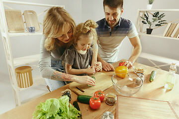 Image showing Cute little girl and her beautiful parents are cutting vegetables in kitchen at home