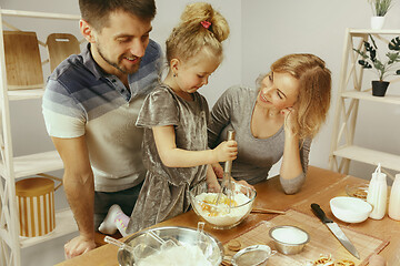 Image showing Cute little girl and her beautiful parents preparing the dough for the cake in kitchen at home