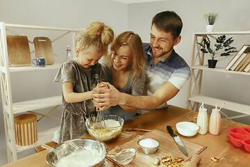 Image showing Cute little girl and her beautiful parents preparing the dough for the cake in kitchen at home