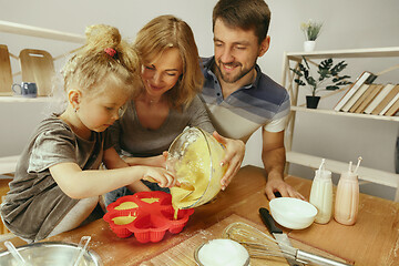 Image showing Cute little girl and her beautiful parents preparing the dough for the cake in kitchen at home