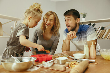 Image showing Cute little girl and her beautiful parents preparing the dough for the cake in kitchen at home