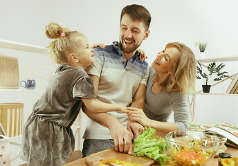 Image showing Cute little girl and her beautiful parents are cutting vegetables in kitchen at home