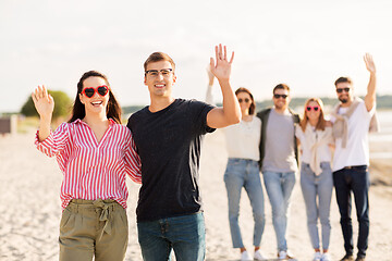 Image showing happy couple with friends waving hands on beach