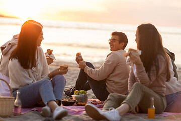 Image showing happy friends eating sandwiches at picnic on beach