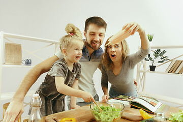 Image showing Cute little girl and her beautiful parents are cutting vegetables in kitchen at home