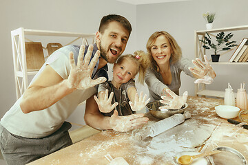 Image showing Cute little girl and her beautiful parents preparing the dough for the cake in kitchen at home