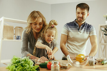 Image showing Cute little girl and her beautiful parents are cutting vegetables in kitchen at home