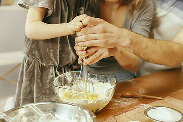 Image showing Cute little girl and her beautiful parents preparing the dough for the cake in kitchen at home