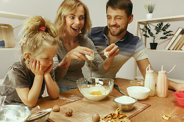 Image showing Cute little girl and her beautiful parents preparing the dough for the cake in kitchen at home