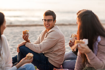 Image showing happy friends eating sandwiches at picnic on beach