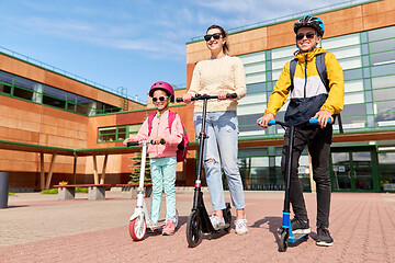 Image showing happy school children with mother riding scooters