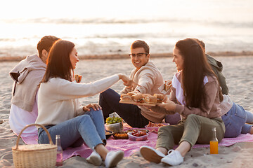 Image showing happy friends eating sandwiches at picnic on beach