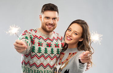 Image showing happy couple in christmas sweaters with sparklers