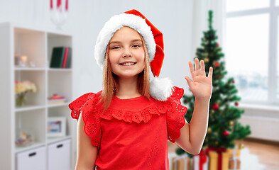 Image showing happy girl in santa helper hat waving hand at home