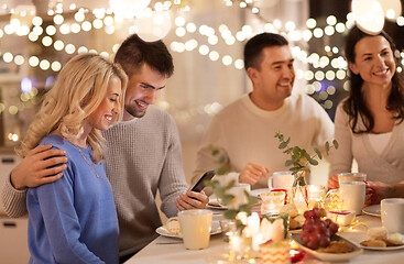 Image showing happy friends with smartphone at tea party at home