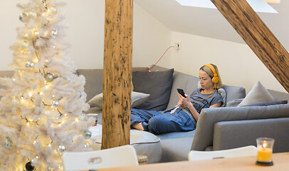 Image showing Young thoughtful woman sitting indoors at home living room sofa using social media on phone for video chatting and staying connected with her loved ones. Stay at home, social distancing lifestyle