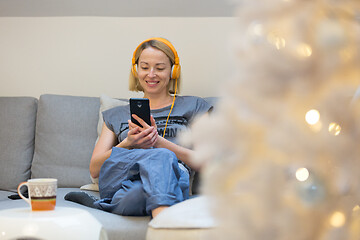 Image showing Young cheerful woman sitting indoors at home living room sofa using social media on phone for video chatting and staying connected with her loved ones. Stay at home, social distancing lifestyle