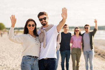 Image showing happy couple with friends waving hands on beach