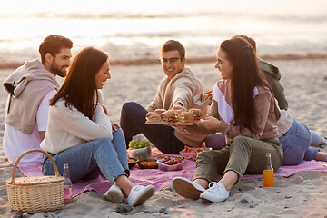 Image showing happy friends eating sandwiches at picnic on beach