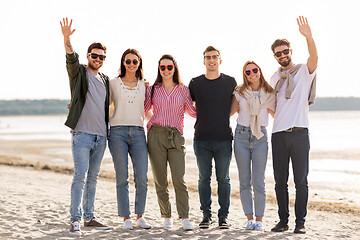 Image showing happy friends waving hands on beach in summer