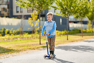 Image showing happy little boy riding scooter in city