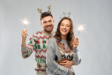 Image showing happy couple in christmas sweaters with sparklers