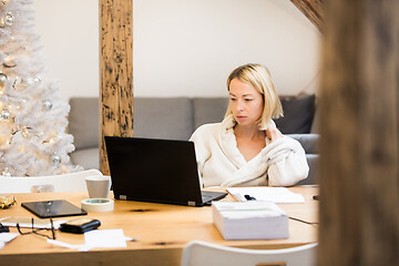 Image showing Young female entrepreneur wearing cosy warm bathrobe working remotly from home in winter Christmas time during 2020 corona virus pandemic. Work from home, selter in place, concept.