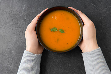 Image showing hands with bowl of pumpkin cream soup on table