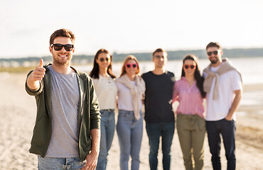 Image showing happy man with friends on beach showing thumbs up