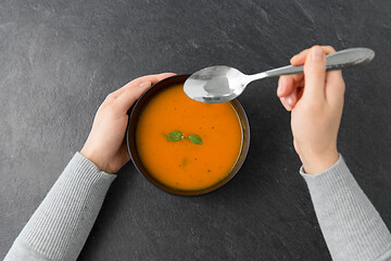 Image showing hands with bowl of pumpkin cream soup on table