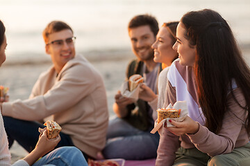 Image showing happy friends eating sandwiches at picnic on beach