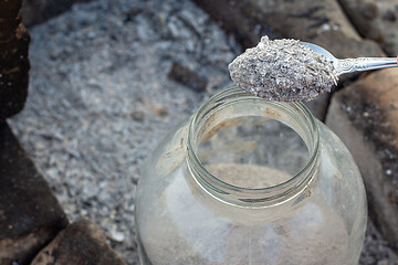 Image showing Spoon pours fresh wood ash into a glass storage jar