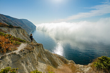 Image showing A girl is standing on a rock who watches the clouds above the sea