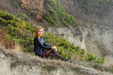 Image showing Beautiful girl in autumn clothes sits in a picturesque place