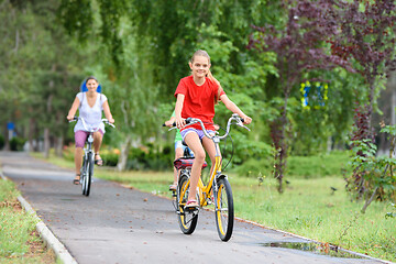 Image showing Girl and mom ride a bike along the alley