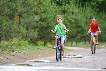 Image showing Two girls ride a bike on a rainy warm day