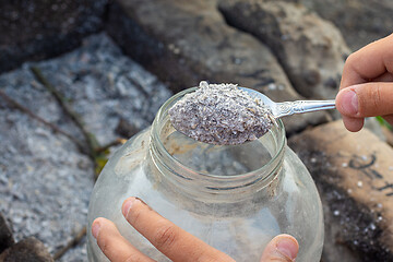 Image showing Hands pouring fresh wood ash into a glass jar