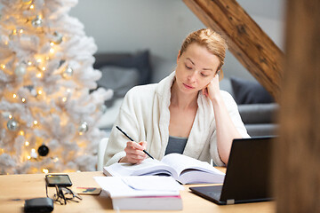 Image showing Young female entrepreneur wearing cosy warm bathrobe working remotly from home in winter Christmas time during 2020 corona virus pandemic. Work from home, selter in place, concept.